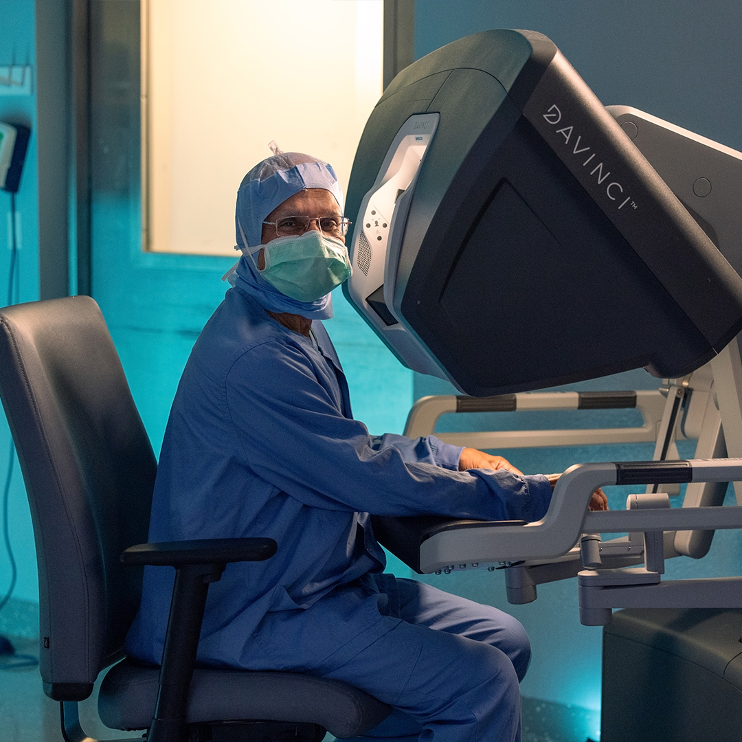 Dr. Sivakumar, a St. Joseph's Health general surgeon, sits at a da Vinci robot in full medical PPE in preparation for surgery.